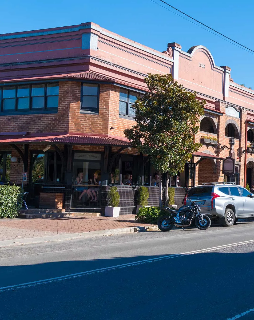 Two-storey brick hotel with arched verandahs and a pink parapet on a sunny main street